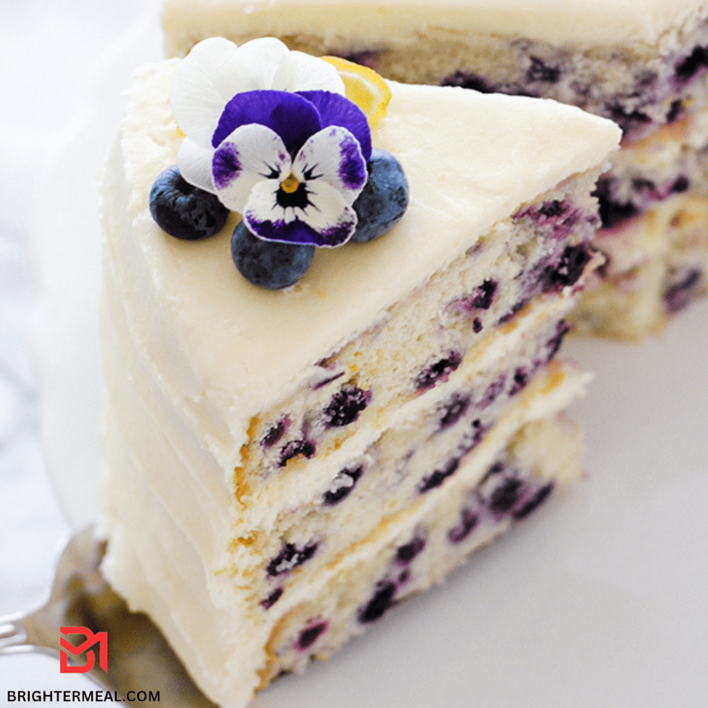 A tempting visual of a freshly baked Blueberry Lemon Creme Cake, showcasing golden-brown perfection. The moist cake is adorned with a generous layer of creamy frosting, dotted with plump blueberries and garnished with vibrant lemon zest. A visual feast that captures the essence of this delectable dessert, inviting you to indulge in a slice of pure bliss